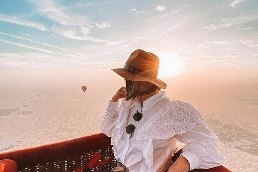 Eine Person mit weißem Hemd und Hut blickt auf eine weite Landschaft, in der Ferne ist eine Heißluftballon zu sehen. 1