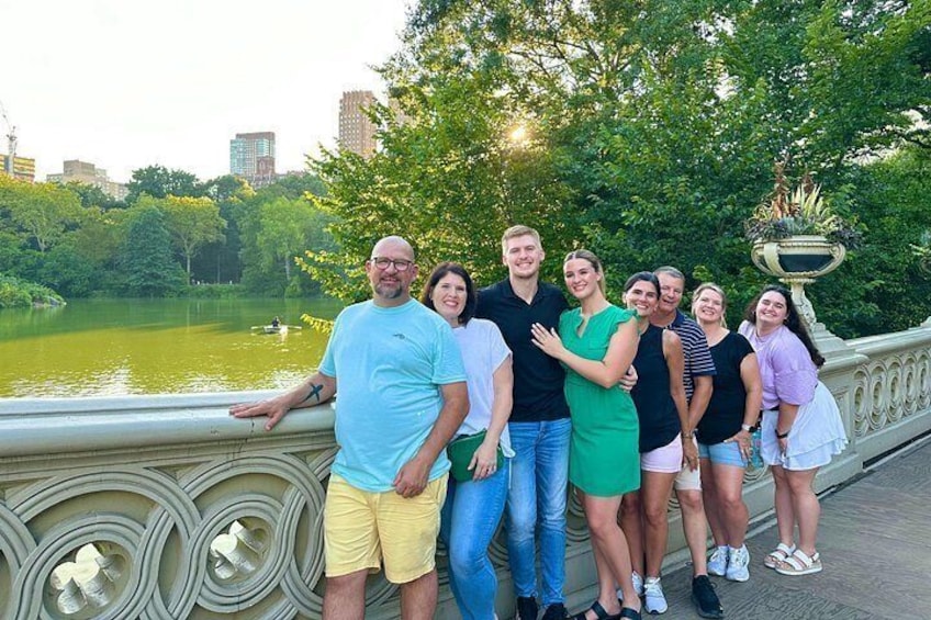 A group of people standing on a bridge with a river and trees in the background. 3