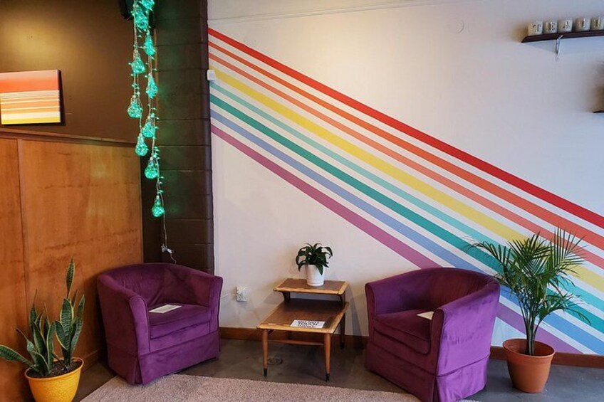 A room with a colorful striped wall, two purple chairs, a small table, and potted plants. 5