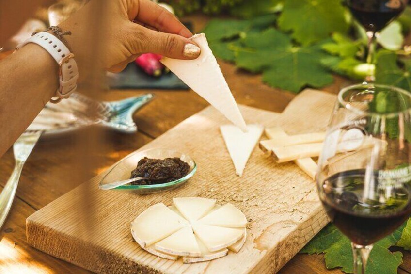 A person holding a napkin, a cheese wheel, a small dish of black olives, and a glass of red wine on a wooden table. 4
