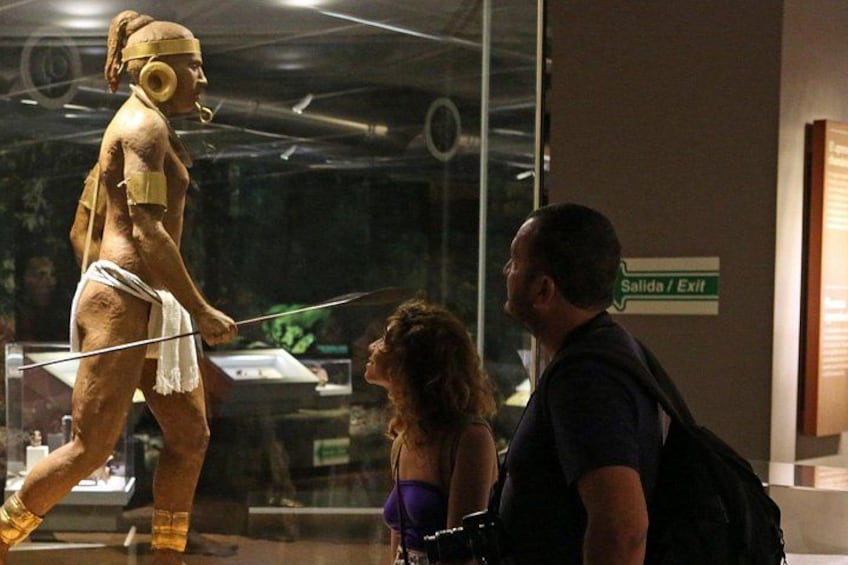 A museum exhibit with a life-sized statue of a figure holding a staff, a glass display case, and a sign indicating an exit. 5