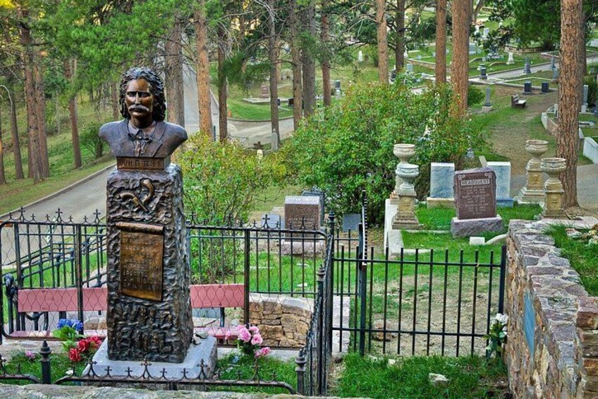 A cemetery with a prominent statue, tombstones, and a well-maintained lawn. 3