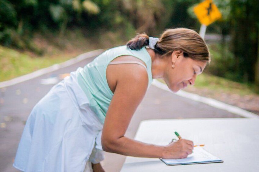 A person writing on a clipboard by the side of a road with a yellow warning sign in the background. 3