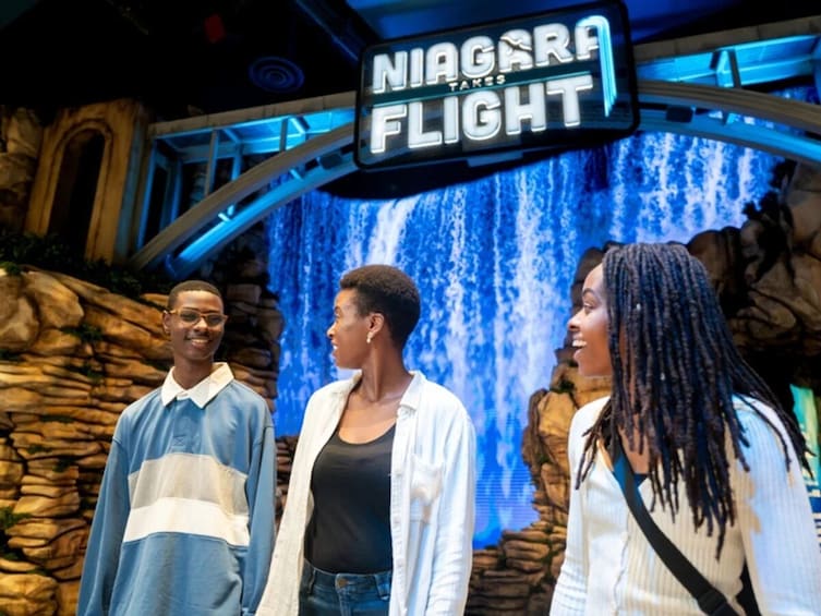 Kolme ihmistä seisoo vesiputousta taustanaan, ja heidän edessään on kyltti, jossa lukee: ”Niagaran lento”. 4