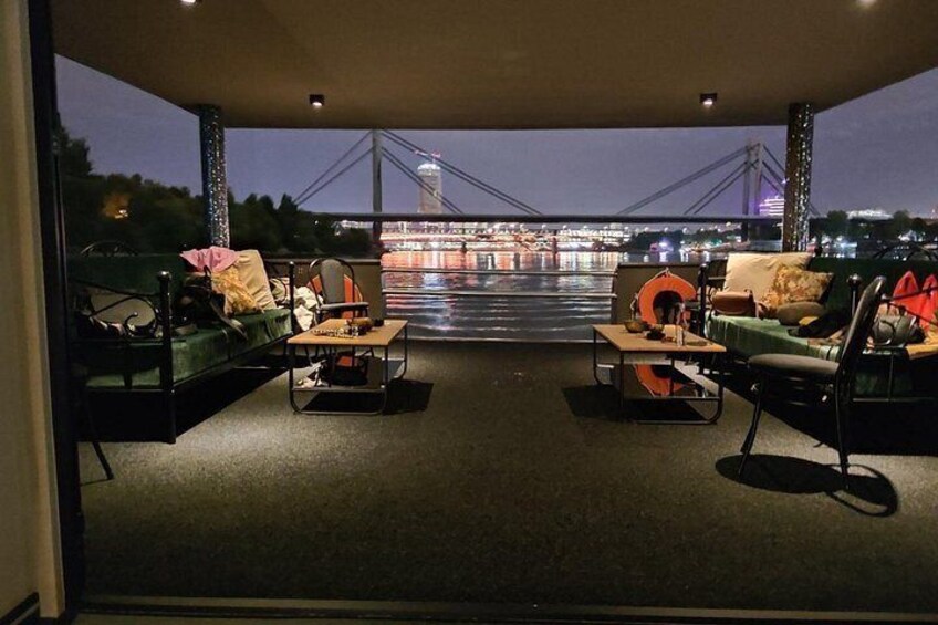 An indoor seating area with sofas and tables, a view of a bridge, and a cityscape at night. 2