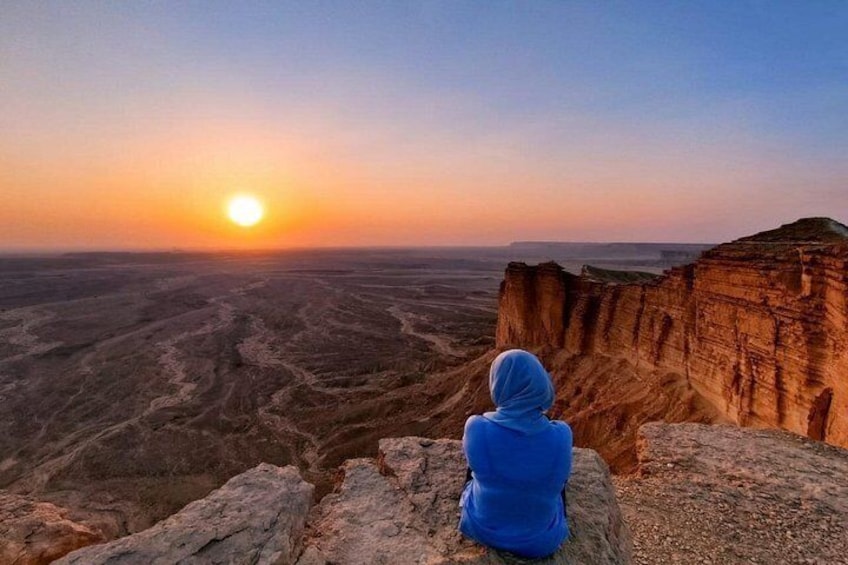 A person sitting on a rock overlooking a vast landscape with a sunset in the background. 1