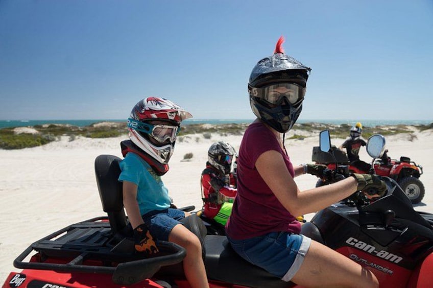 Dos personas en un cuatrimoto rojo sobre una playa arenosa, con dunas al fondo. 4