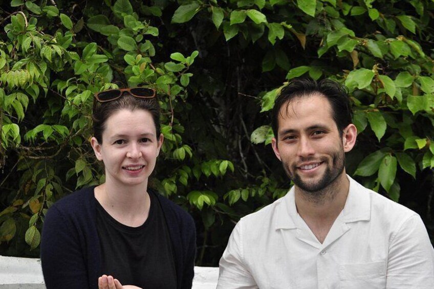 Two people sitting outdoors with green foliage in the background. 4