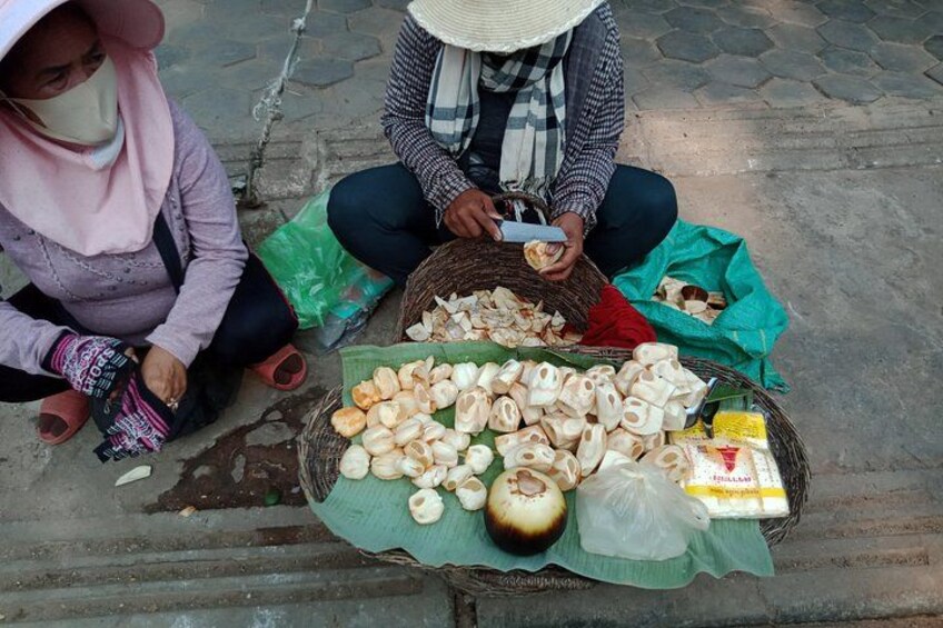 Two people sitting on the ground with baskets of food items, including what appears to be dried fruits and nuts. 3