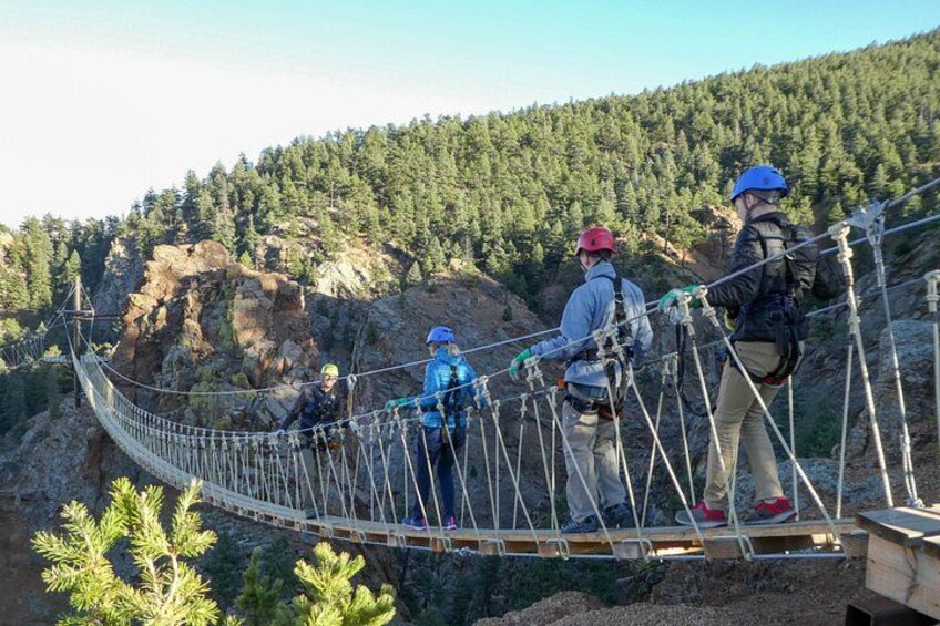 People on a suspension bridge with a forested mountain backdrop. 1