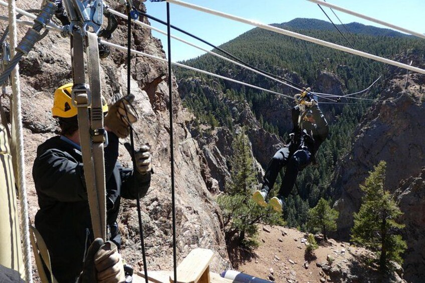 A person bungee jumping with safety gear, another person assisting, and a mountainous landscape with trees. 2