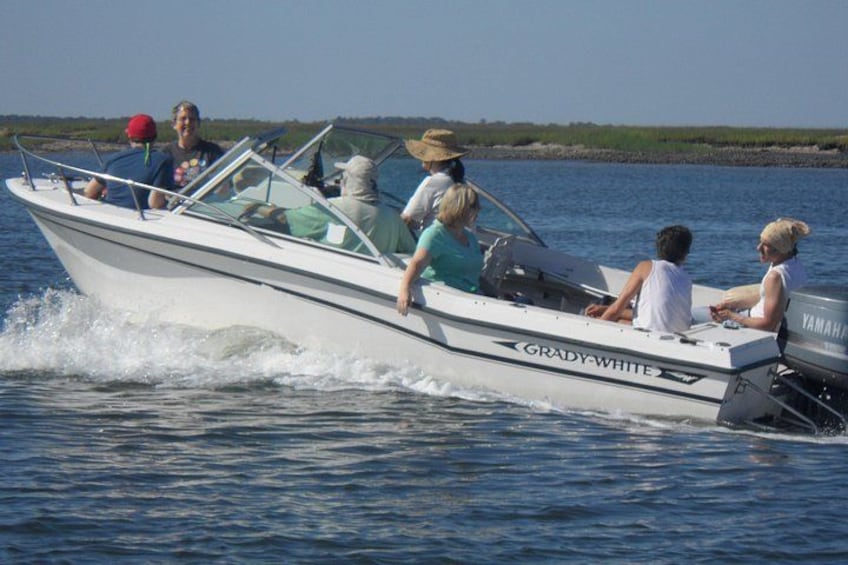 A white boat with the name 'GRADY-WHITE' on the side, moving on water with people on board. 2