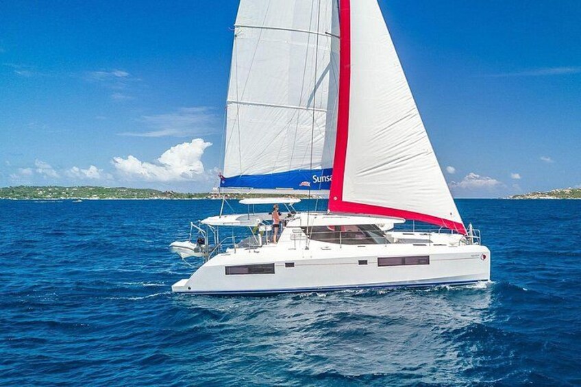 A white sailboat with a red stripe on the sail, sailing on blue water. 1