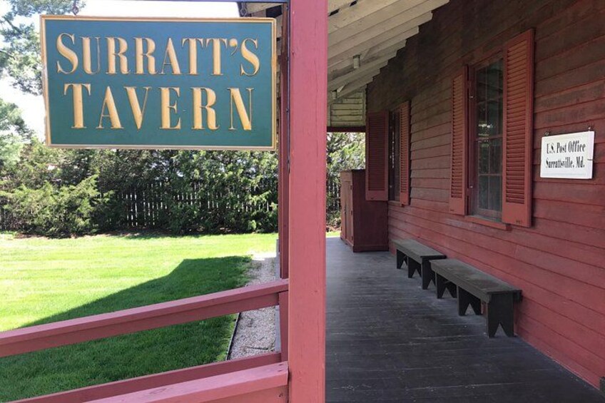 En byggnad av trä med en skylt som visar texten ”Surratt’s Tavern” och en skylt för ett amerikanskt postkontor. 3