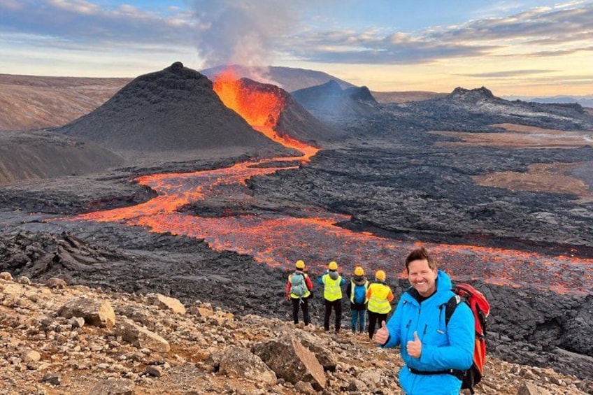 Ett vulkaniskt landskap med flytande lava, en grupp vandrare och en person i förgrunden. 1