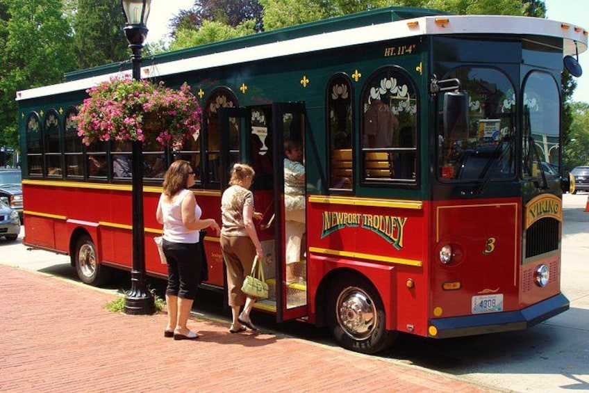 A vintage trolley with floral decorations, passengers boarding, and a brick pavement. 1