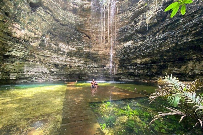 A natural cave with a waterfall, clear water, and lush greenery. 1