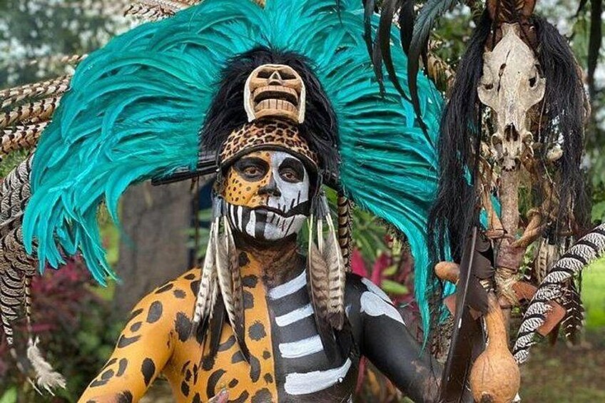 A person in a costume with a large feathered headdress, a skeleton prop, and a leopard print outfit. 2