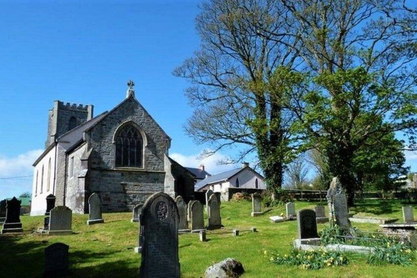 Una iglesia con fachada de piedra, un árbol grande y varias lápidas en un cementerio. 2