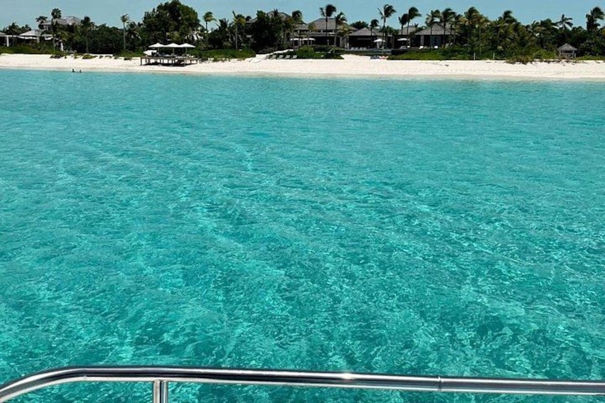 A clear turquoise sea, a white sandy beach, and a row of houses with palm trees in the background. 3