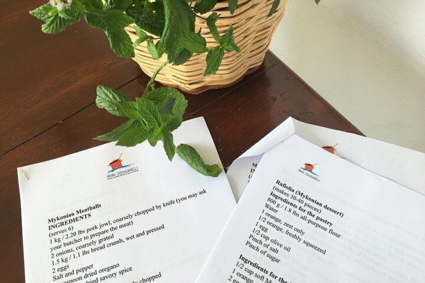 Dos tarjetas de recetas con ingredientes para albóndigas y un postre, sobre una mesa de madera con una planta en maceta al fondo. 5