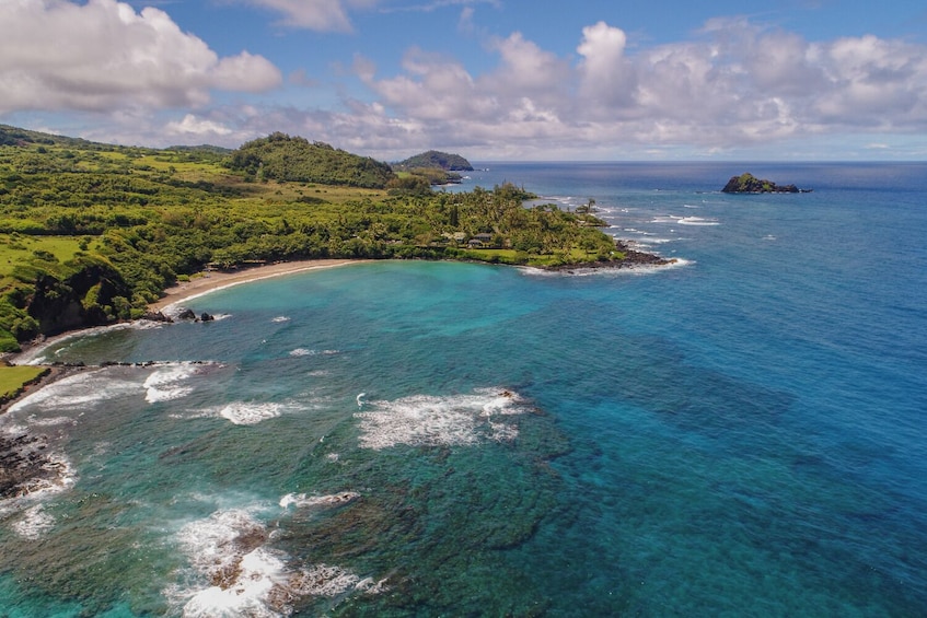 A coastal landscape with a clear turquoise sea, a sandy beach, and lush green hills. 5