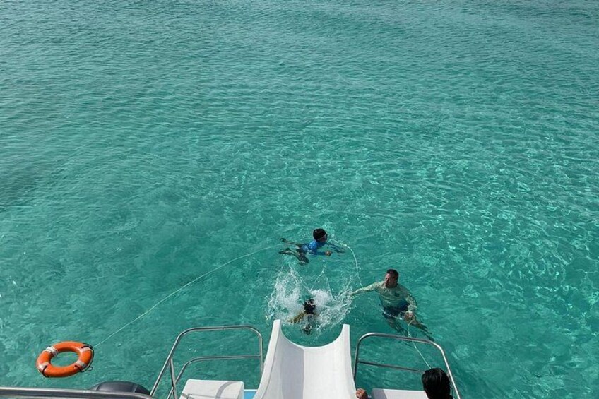 A boat in clear turquoise water with people swimming and a lifebuoy visible. 4