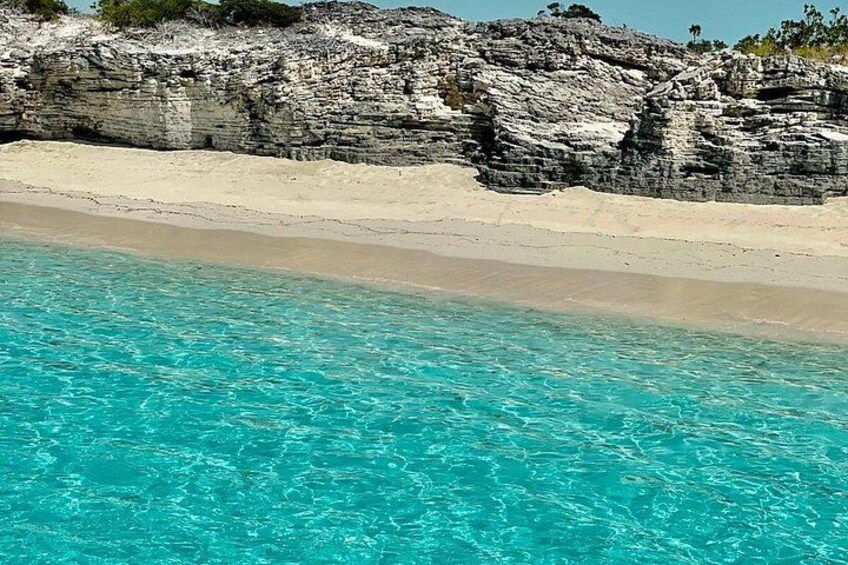 A beach with clear turquoise water, white sand, and rocky cliffs. 2