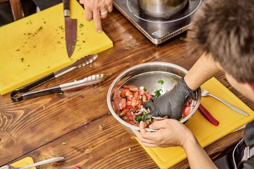 Une personne prépare des aliments, elle coupe des tomates sur une planche à découper en bois, avec un couteau et une pince à proximité. 2
