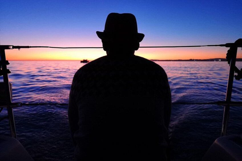 A silhouette of a person wearing a hat, standing on a boat with a sunset in the background. 3