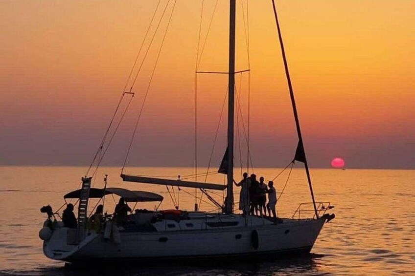 A sailboat with people on deck during sunset. 4
