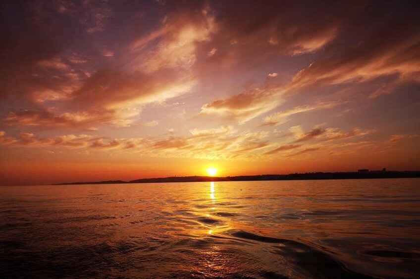 A sunset over a calm body of water with a visible horizon line and distant landforms. 4