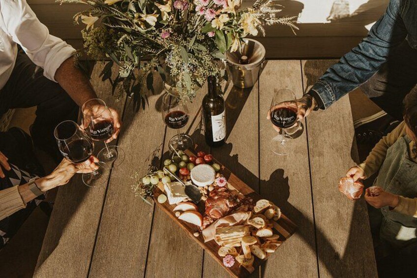 Un tavolo di legno con una bottiglia di vino, bicchieri e un tagliere con formaggi e pane. 2