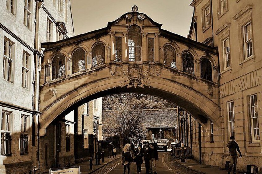 Un pont en pierre orné, doté d’allées en arc de cercle et de nombreuses fenêtres, enjambant une rue où circulent des pi étons et un véhicule. 1