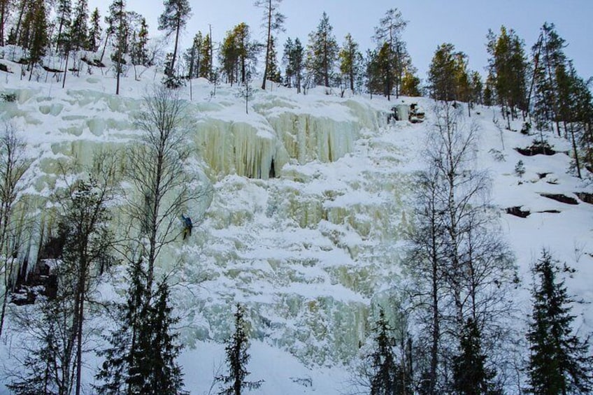 A frozen waterfall with a person climbing it, surrounded by snow-covered trees. 4