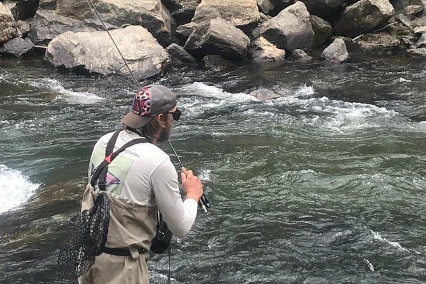 A person fishing in a river with rocks in the background. 4