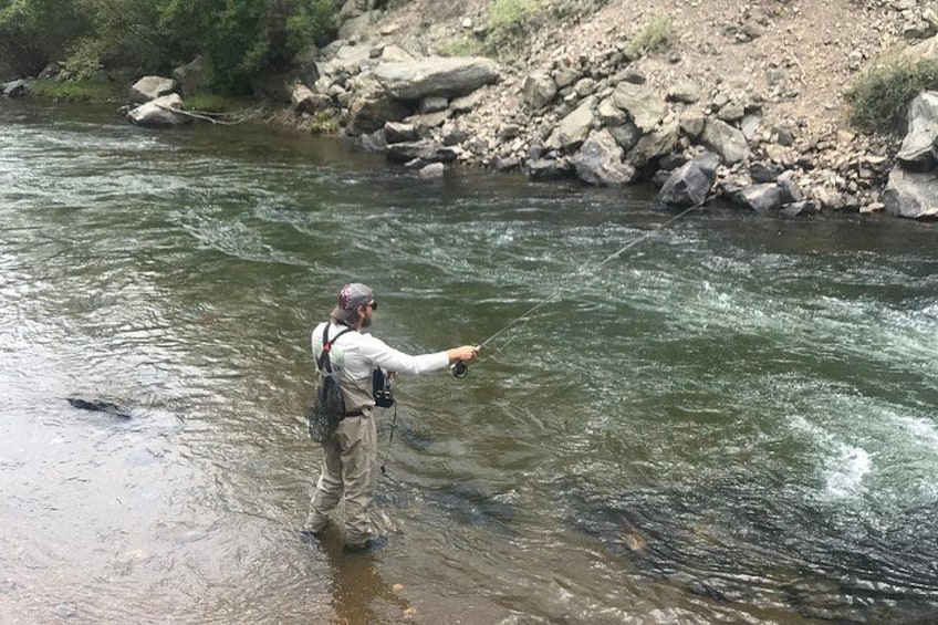 A person standing in a river, holding a fishing rod. 1