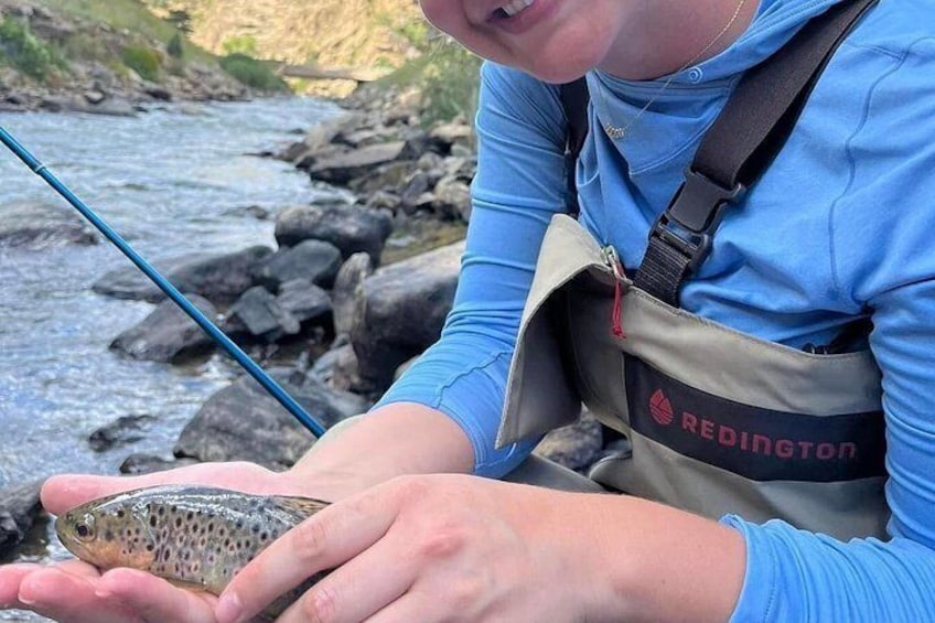 A person holding a fish near a river. 2