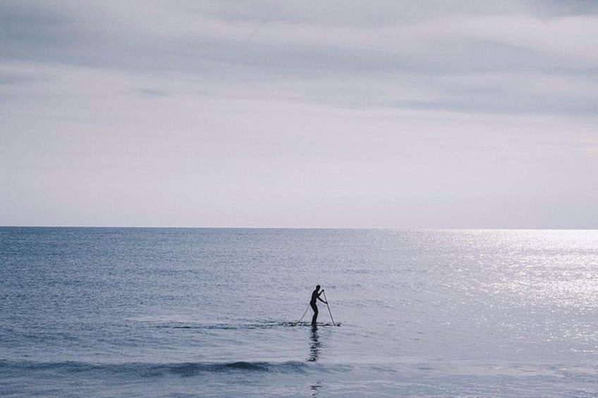 A person paddleboarding on a calm sea under a cloudy sky. 2