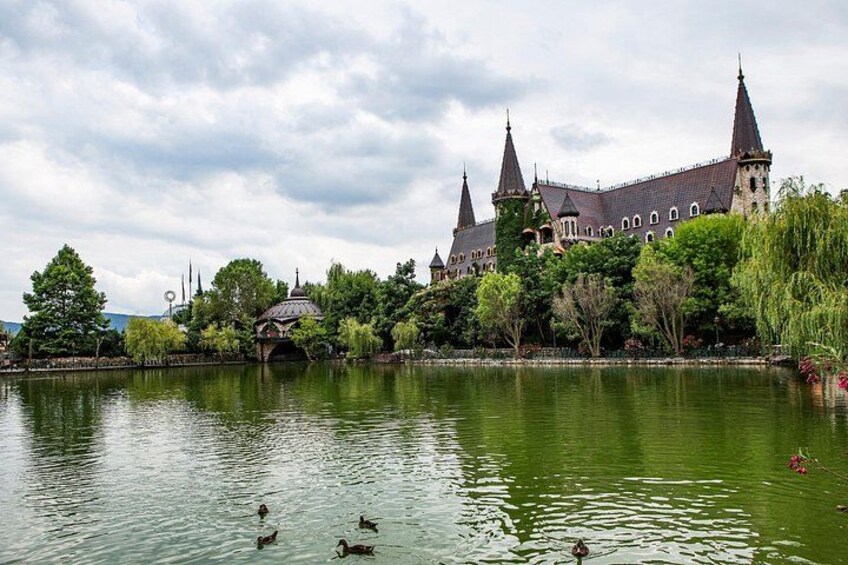 A castle with multiple towers, a body of water with ducks, and lush greenery. 5
