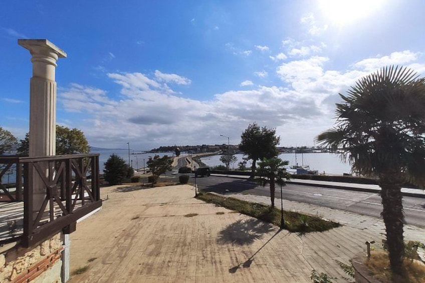 Una passeggiata lungomare con una palma, un pilastro e vista su un ponte e barche. 2