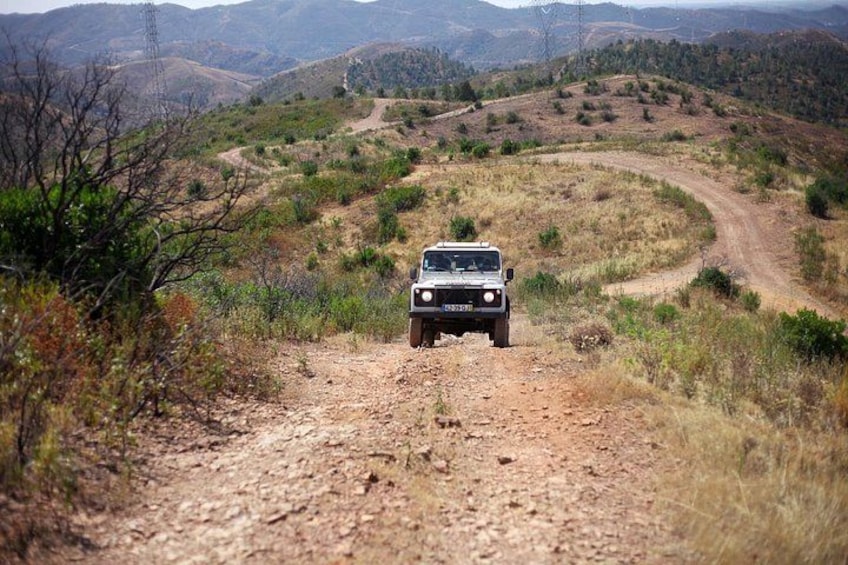 A vehicle on a dirt road surrounded by hills and sparse vegetation. 3