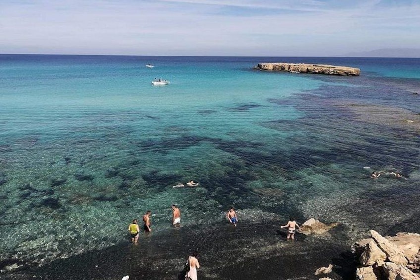 A coastal scene with clear turquoise water, rocky shore, and a distant rocky outcrop. 2
