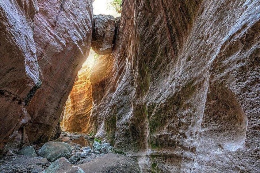 A narrow canyon with rocky walls and a small stream at the bottom. 1