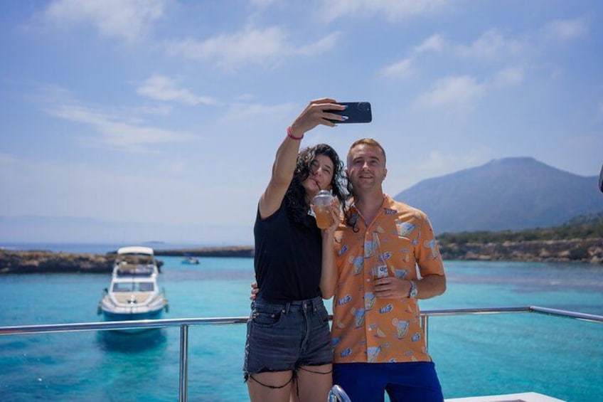 Two people taking a selfie on a boat with a clear blue sea and a boat in the background. 5