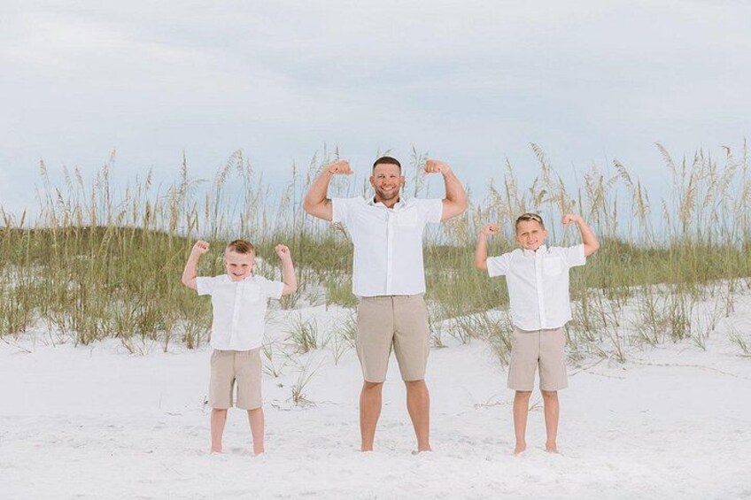Three people standing on a sandy beach with tall grass in the background. 5
