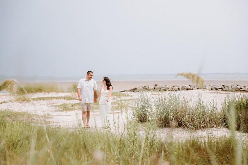 A couple walking on a beach with sand dunes and grasses in the foreground. 4