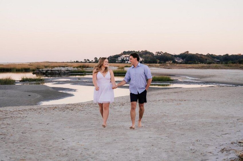 A couple walking on a sandy beach with water in the background. 3