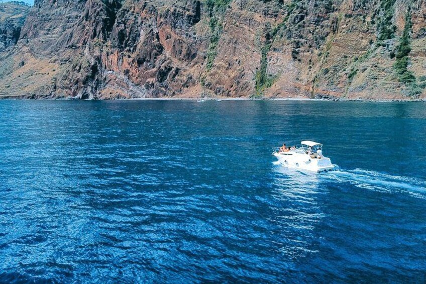 Ein Boot auf ruhiger See mit felsigen Klippen im Hintergrund. 3