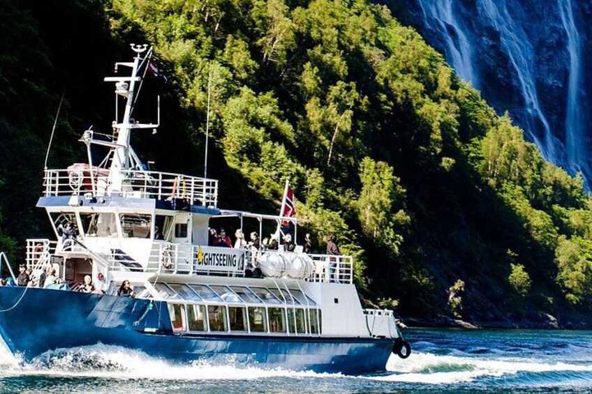 Un bote con la leyenda 'Sightseeing' navegando por un cuerpo de agua, con una cascada y un área boscosa al fondo. 1